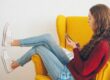 Teenage girl curled up in a yellow armchair scrolling on her phone